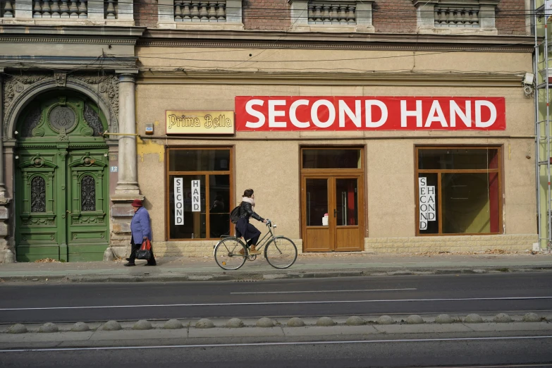 two people walking their bicycles past a second hand store