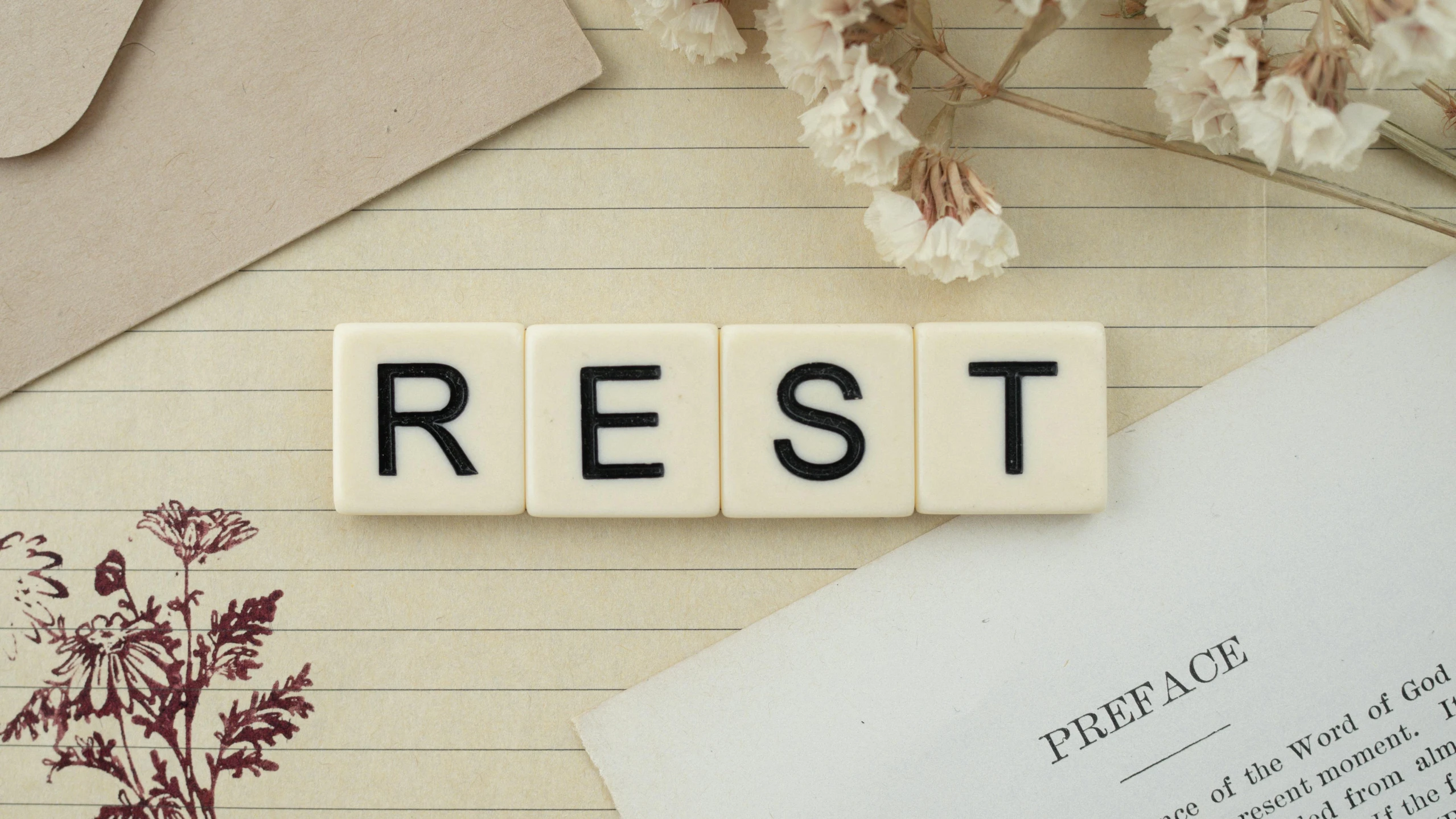 a word spelled on tile type blocks, with papers and dried flowers in background