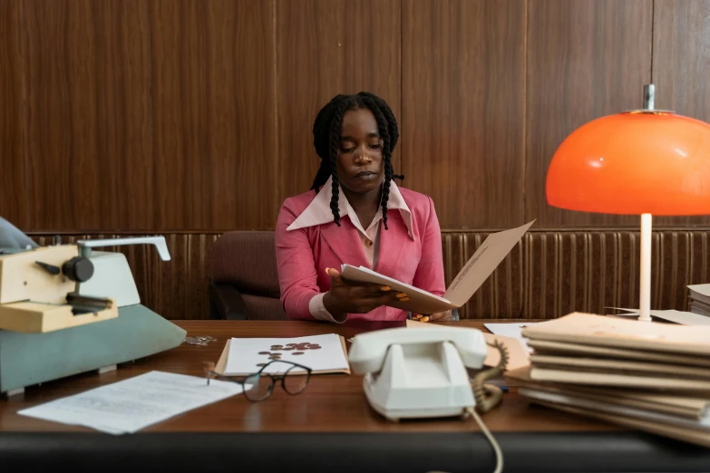 woman sitting at a desk next to a pile of papers and typewriter