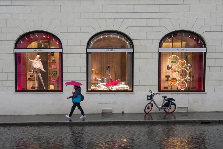 a woman walks down the street past shops with their umbrellas