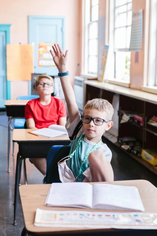 a boy in glasses waves while sitting at his desk