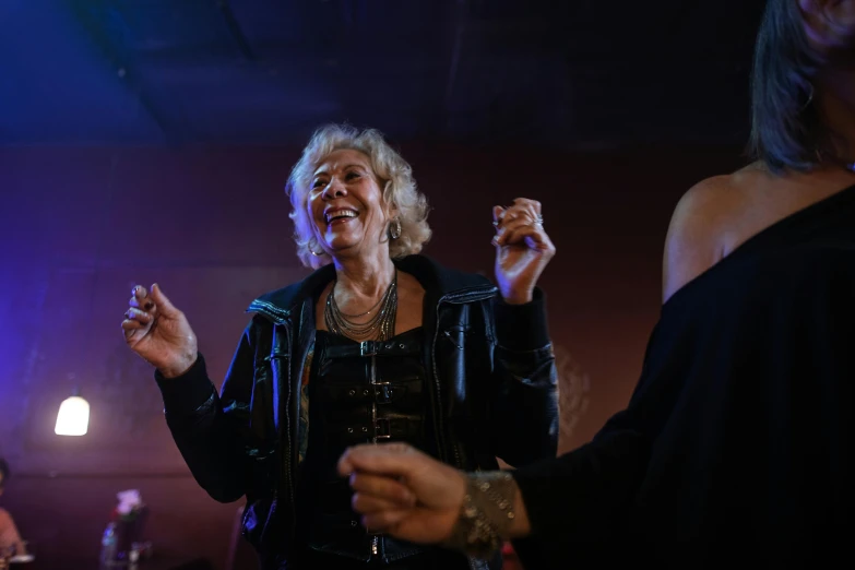 woman wearing a black jacket and a silver chain standing in a room with other women