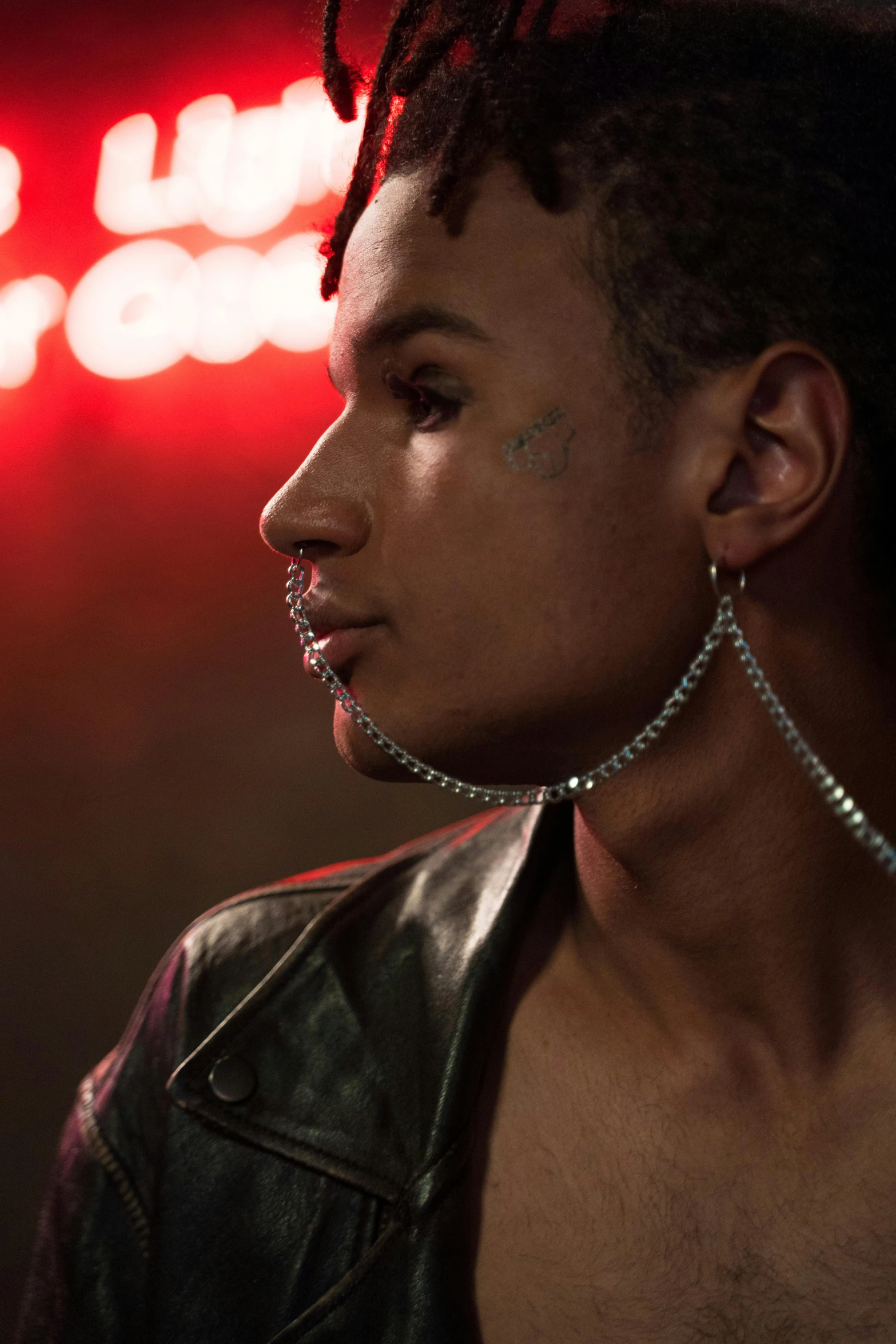 a man with big hoop earring and spiked piercings standing in front of a neon sign