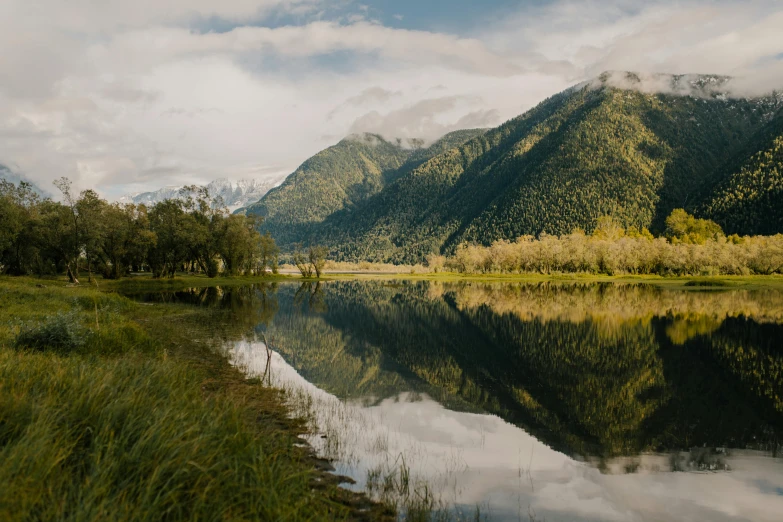 mountains and trees surrounding the water with some clouds in the sky