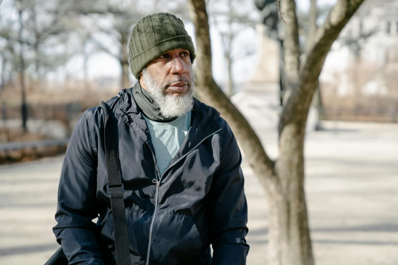 an older man in a green hat is standing near a tree