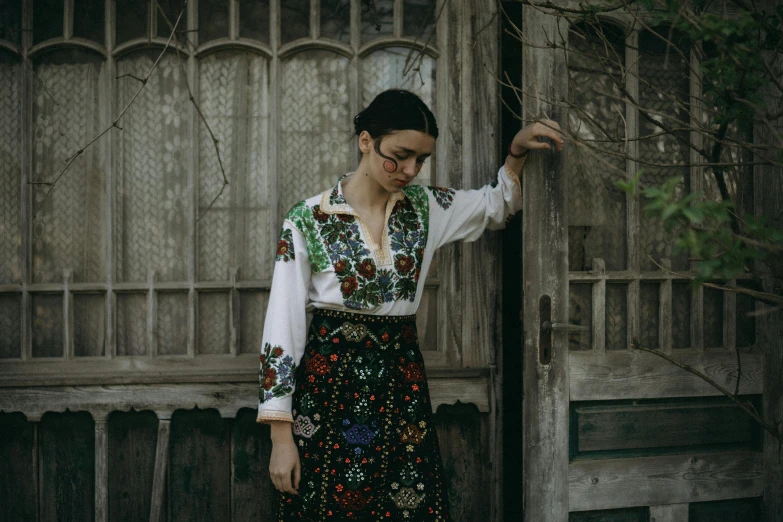 a woman wearing a colorful dress and standing next to a wooden gate