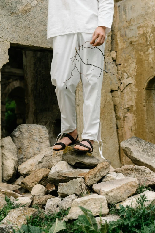 a man in white pants standing on a rock pile