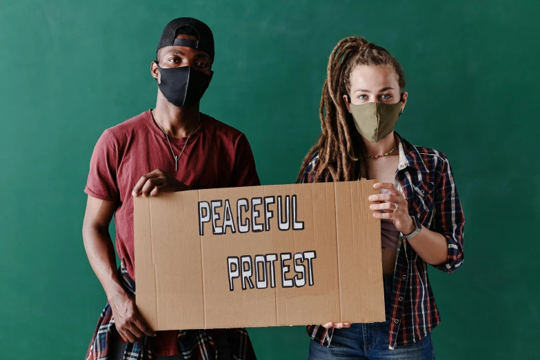 two people with masks are holding a cardboard sign