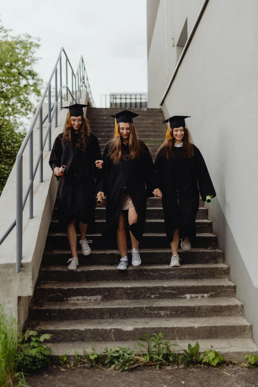 three young ladies dressed in graduation clothes are going down the stairs