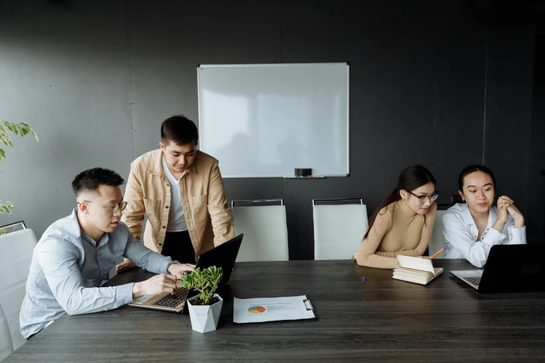 five men and women sitting around a table, looking at laptops