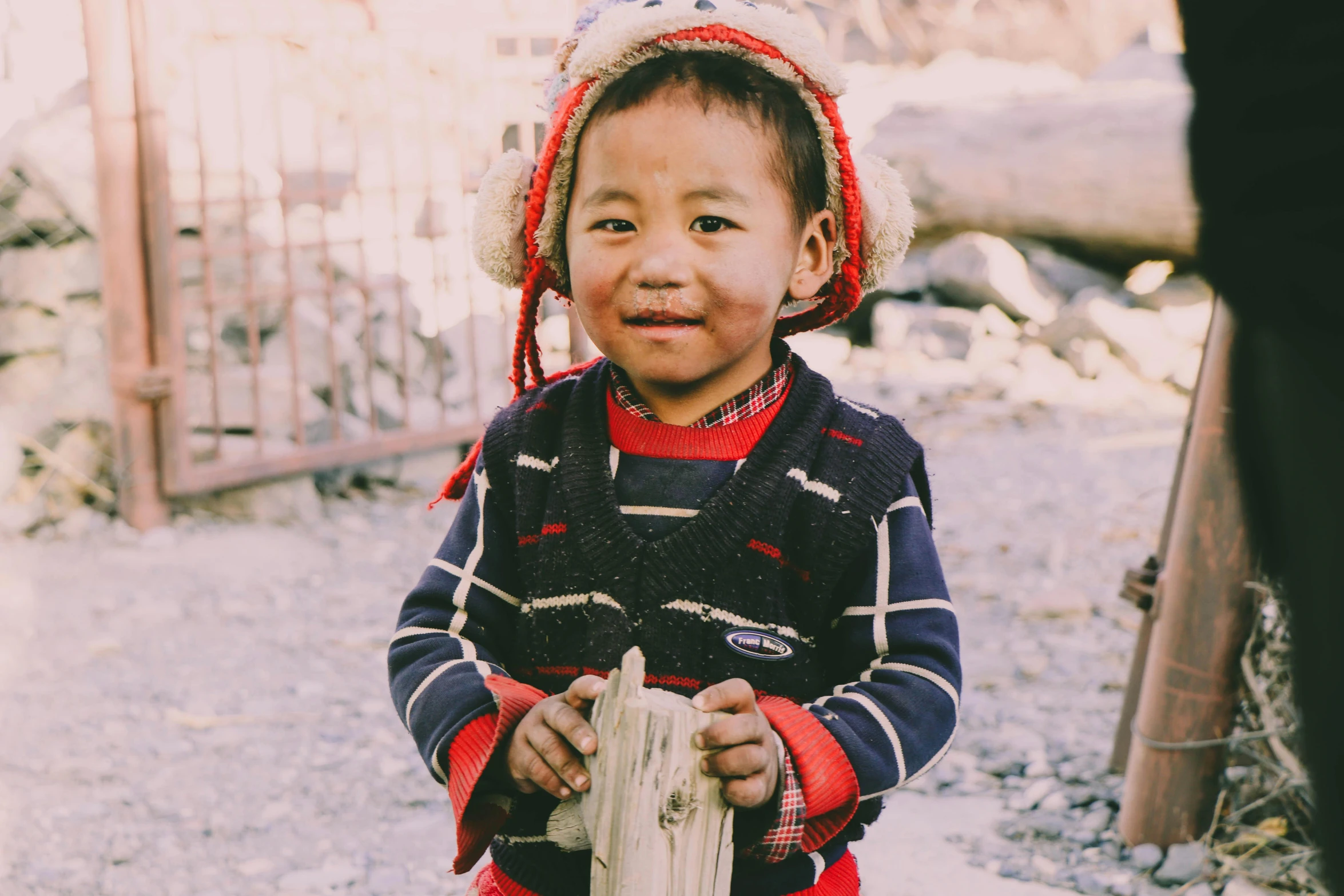 a little  is smiling while holding a fence