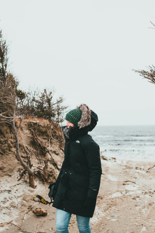 a woman wearing a green hat walking down the beach