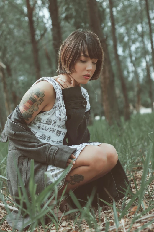 a person sitting in the woods with tattoos on their arm