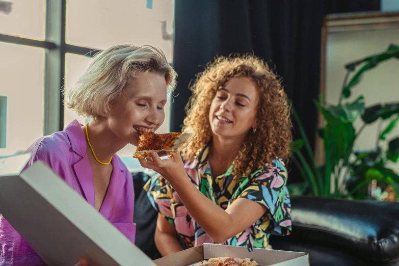 two woman eating pizza in a box