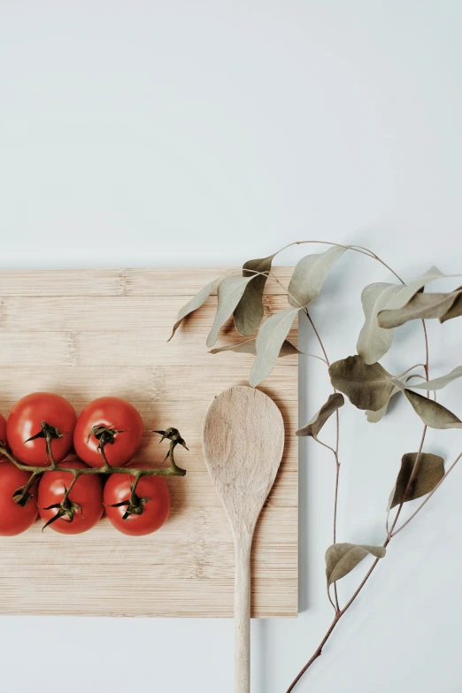 a wooden board with four tomatoes and a wooden spoon