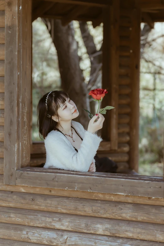 a woman in white sweater holding a red flower