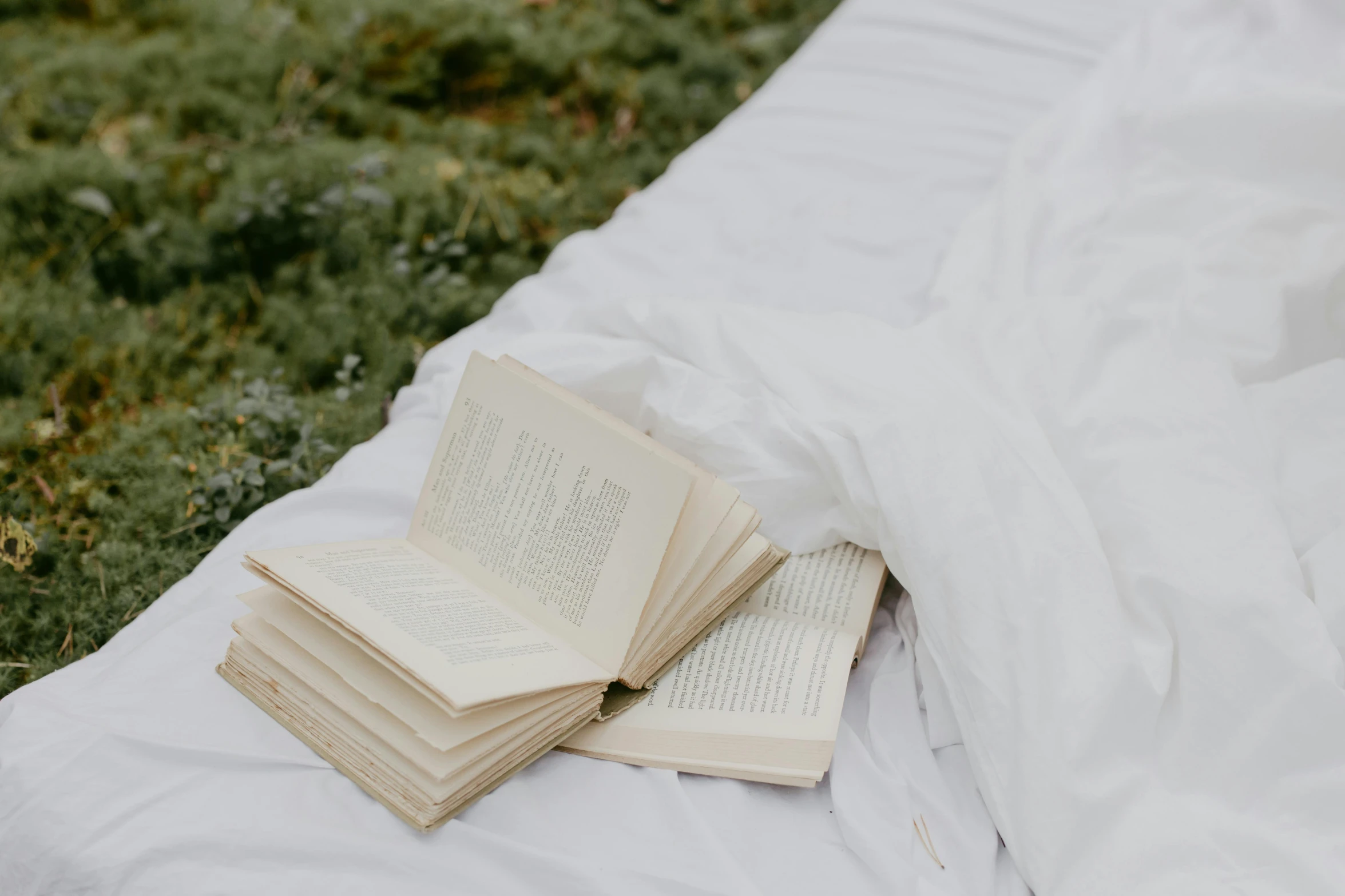 an open book on a white blanket next to green grass