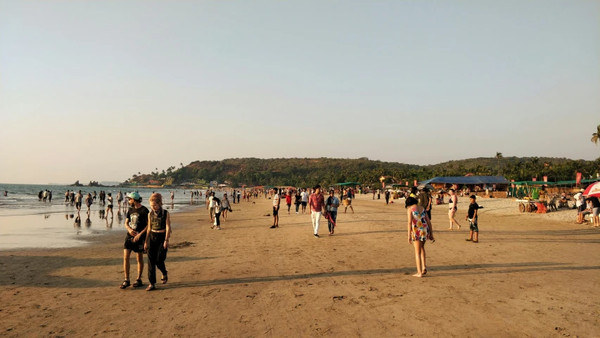 several people walking on the beach next to some trees