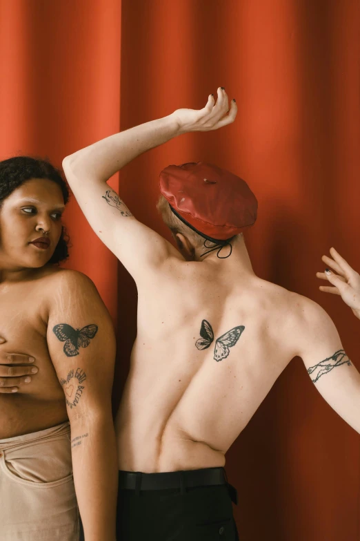 two women pose while their backs are covered with tattoos