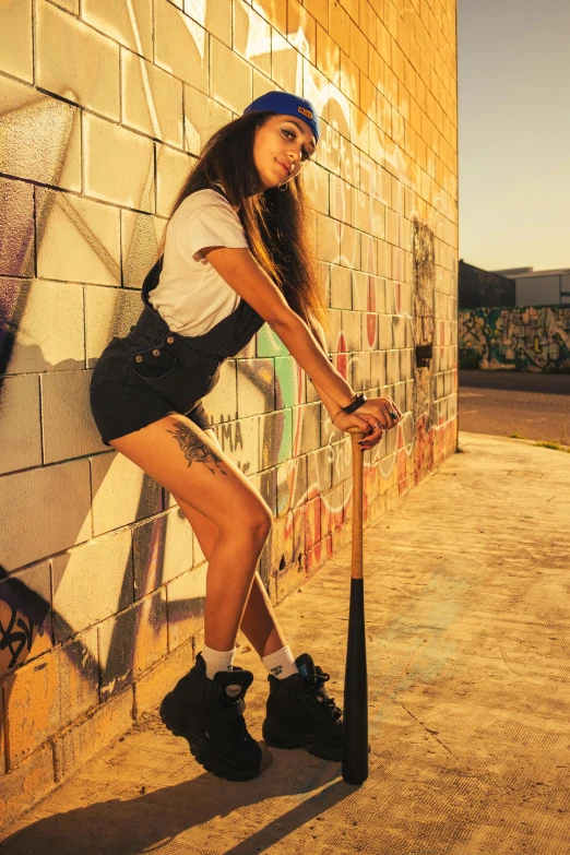 a woman leaning against a brick wall with a baseball bat