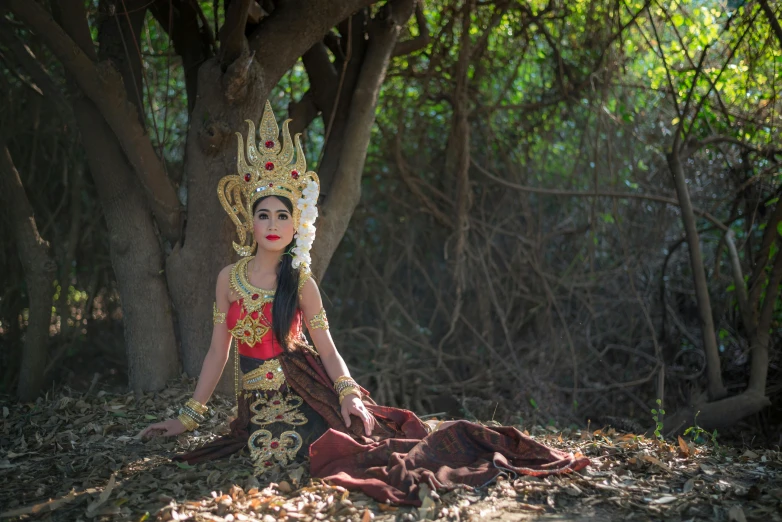 woman in costume sitting on forest floor under tree