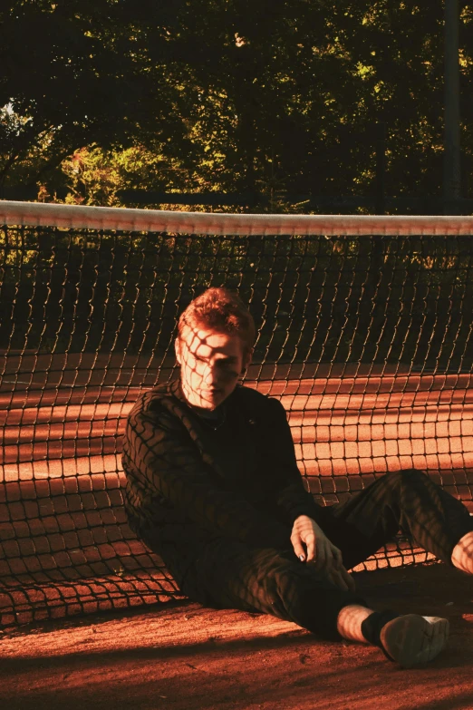 a man sitting on the ground under a tennis net