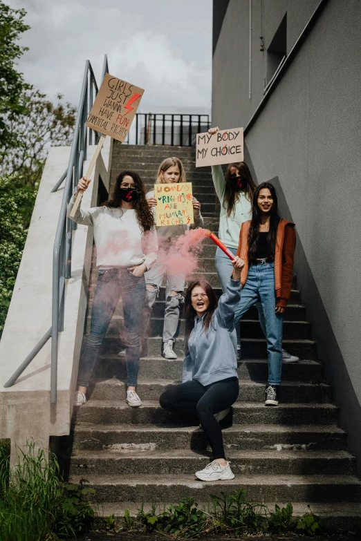 five teenage girls are standing on some stairs and holding signs