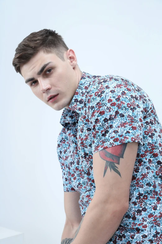 a young man with a tattoo on his arm is wearing floral print shirt