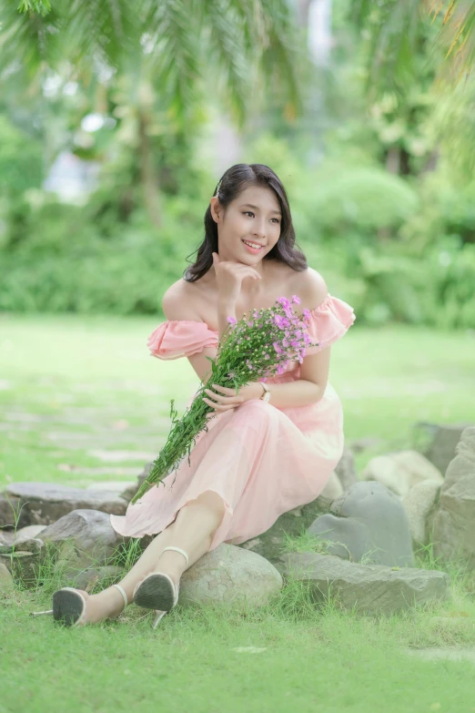 a beautiful woman sitting in a grass field holding flowers
