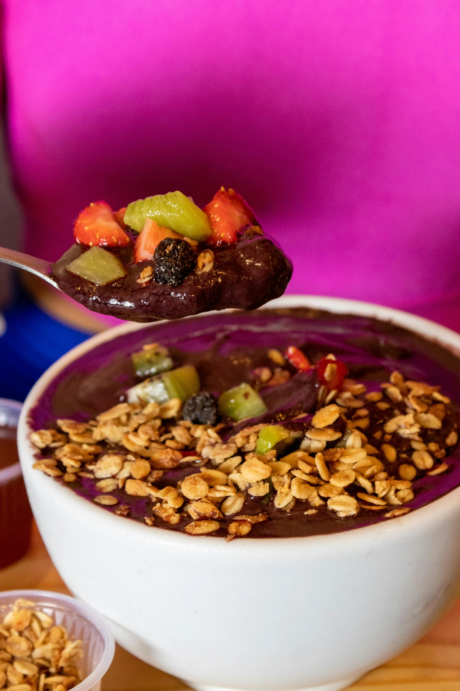 bowl of food on wooden table and person holding a spoon in it