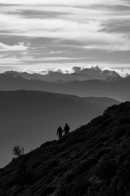 two people hiking up a hill under cloudy skies