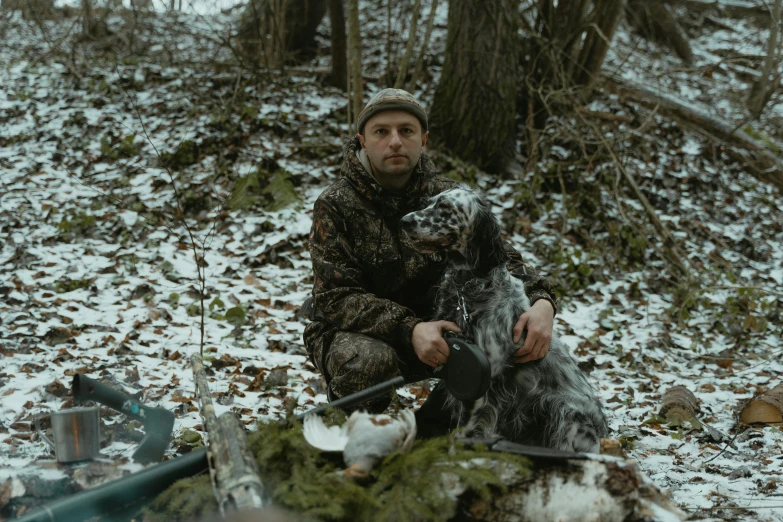 a man kneeling down with a dog next to it in the snow