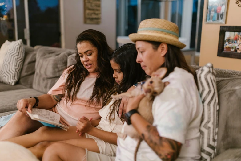 three people sit on a couch with a cat next to them