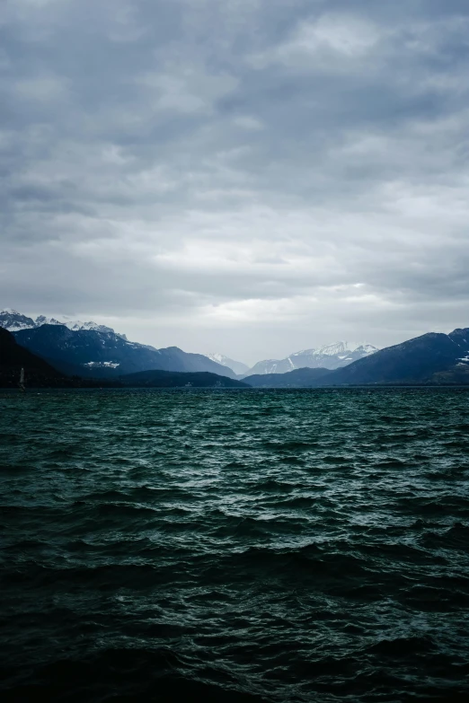 clouds are rolling over the mountain range as the water is almost calm