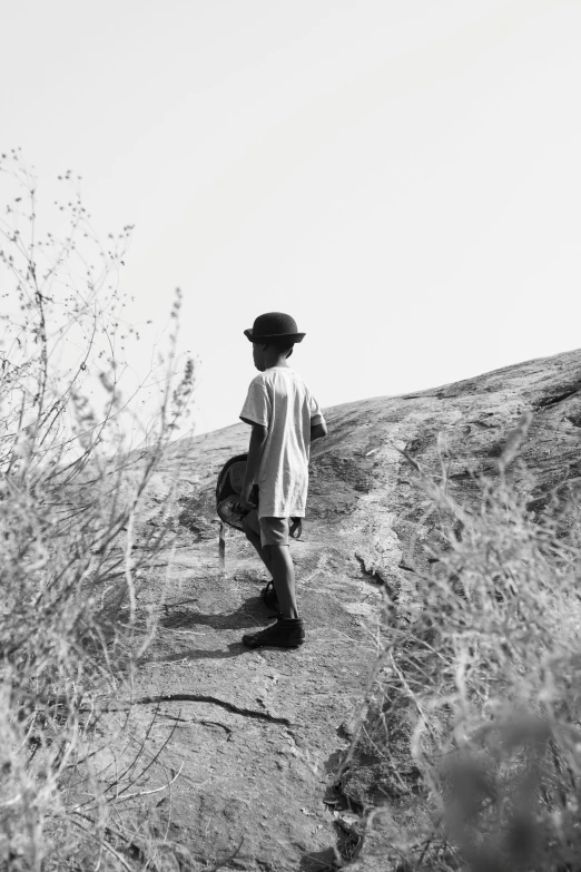 a person standing on top of a hill wearing a hat and carrying a bag