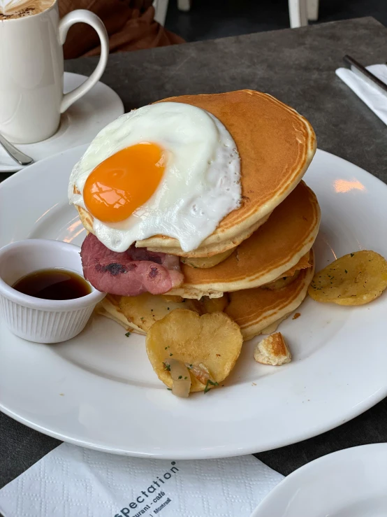 a stack of pancakes on a white plate with eggs