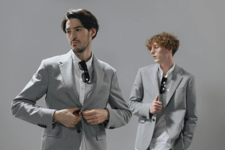 a man adjusting his suit while another man adjusts his tie
