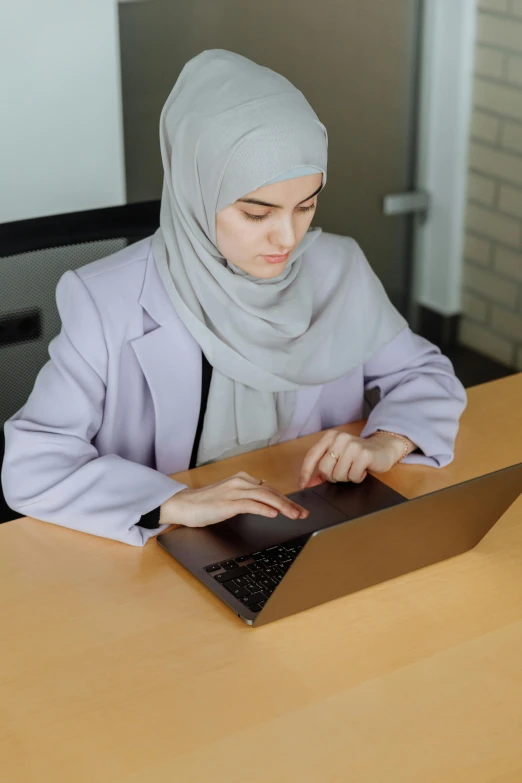 a woman in gray shirt sitting at table with laptop