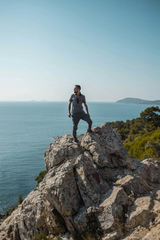 a man posing on top of a rocky hill by the ocean