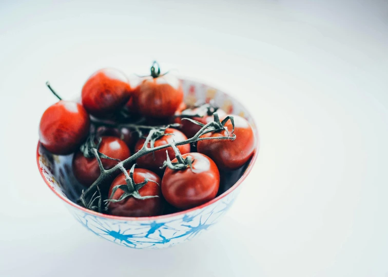 a bowl filled with red tomatoes on top of a table