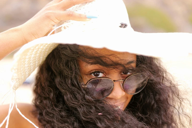 a woman in sunglasses and a white hat smiles