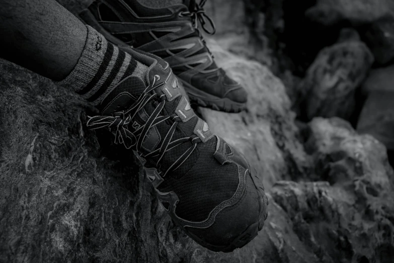 a black and white po of a man's feet wearing hiking shoes on some rocks