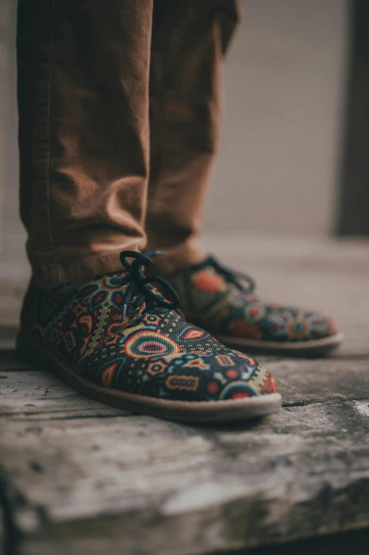 the shoes are colorfully embroidered and have a pair of legs standing beside it