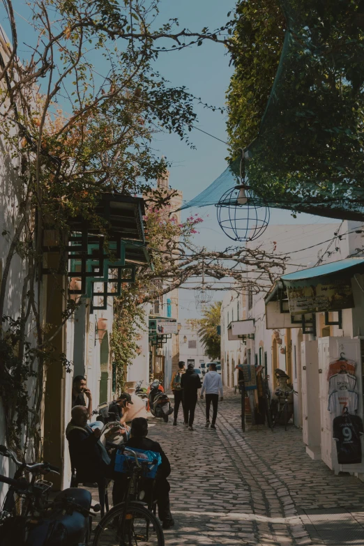 a narrow street with people sitting and walking on it