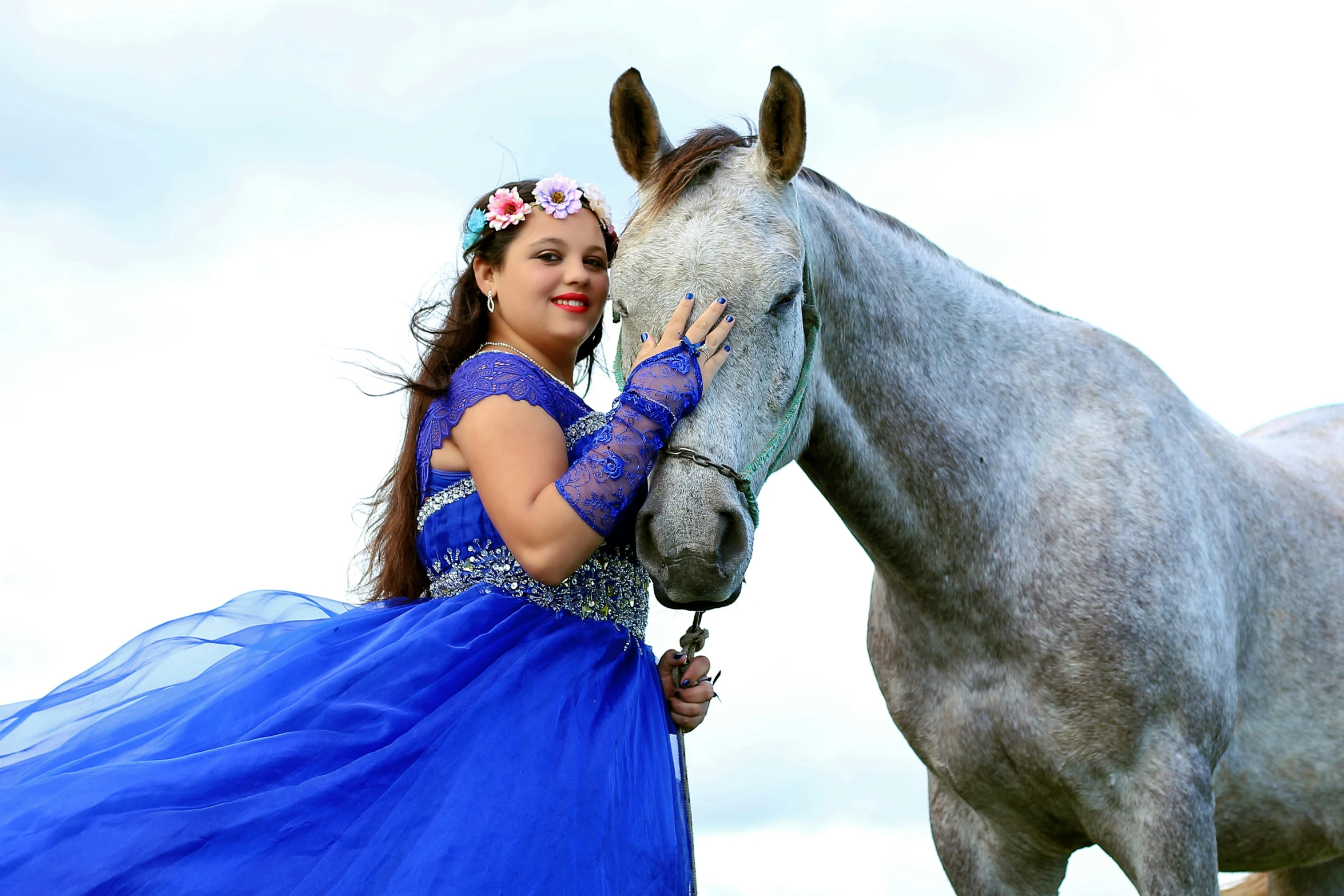 a pretty young lady in a blue dress petting a horse