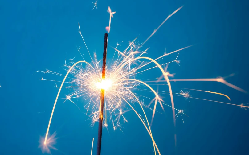 a small sparkler with sparks and blue sky in the background