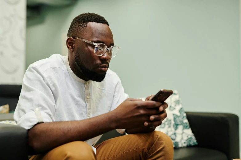 a man sitting on a couch, looking at his cell phone