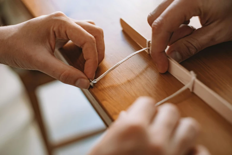 two hands on a piece of wood tying twine