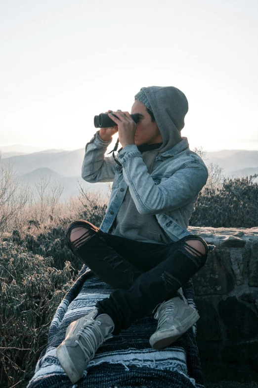 a woman taking pos with her phone while sitting in the wilderness