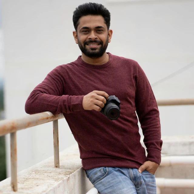 a smiling man poses next to a railing with his camera